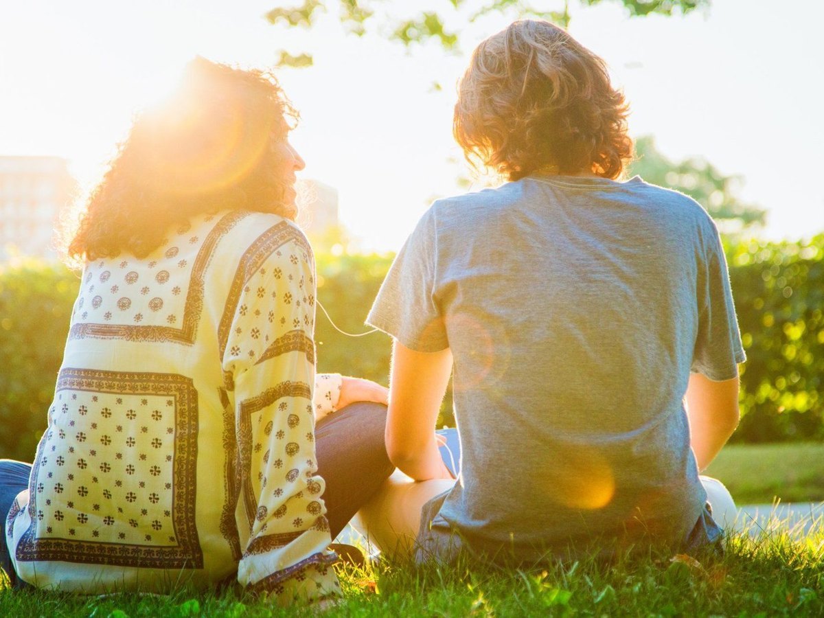Two people sitting together on the grass in a park at sunset, talking