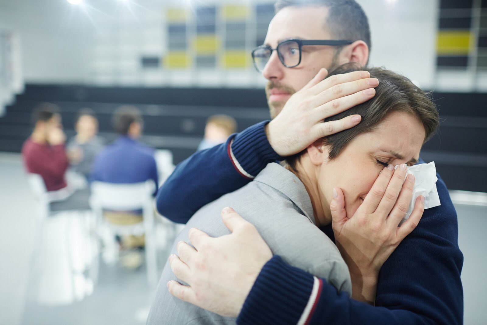 A man comforting a woman in tears during a group session, his hand resting on her head