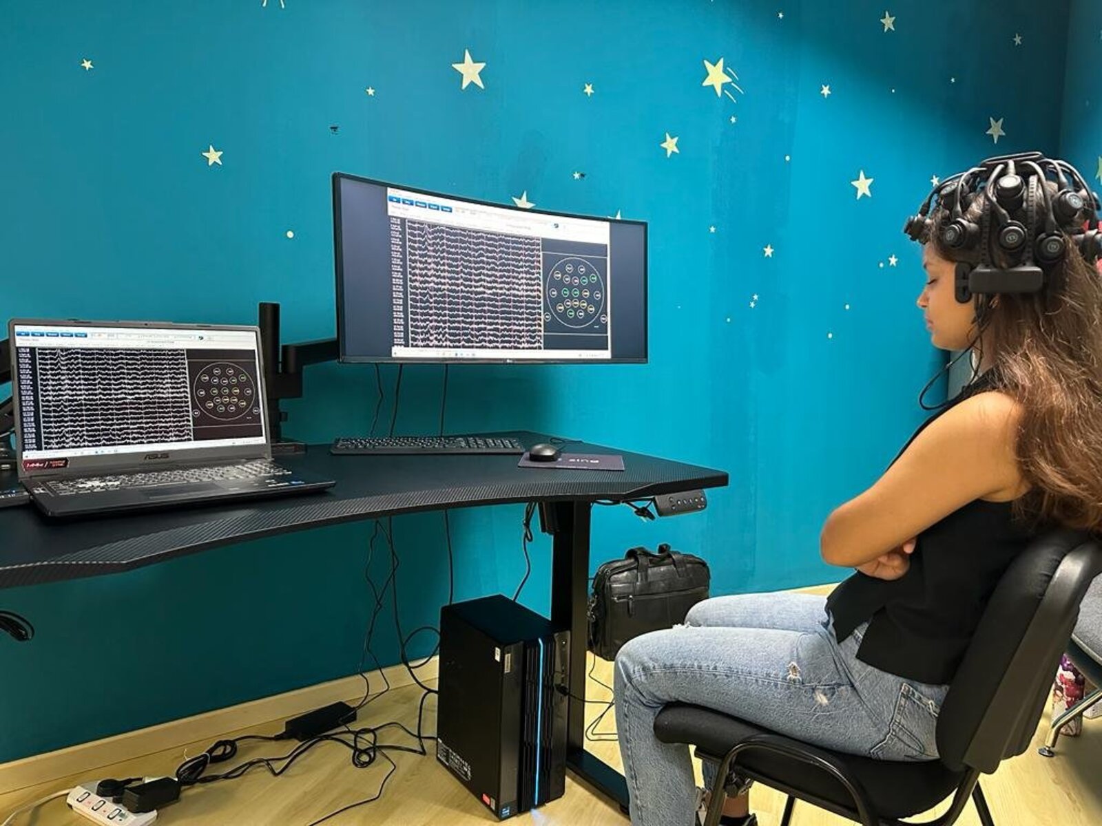A client in a neurofeedback session, brainwave activity displayed on the screens beside her