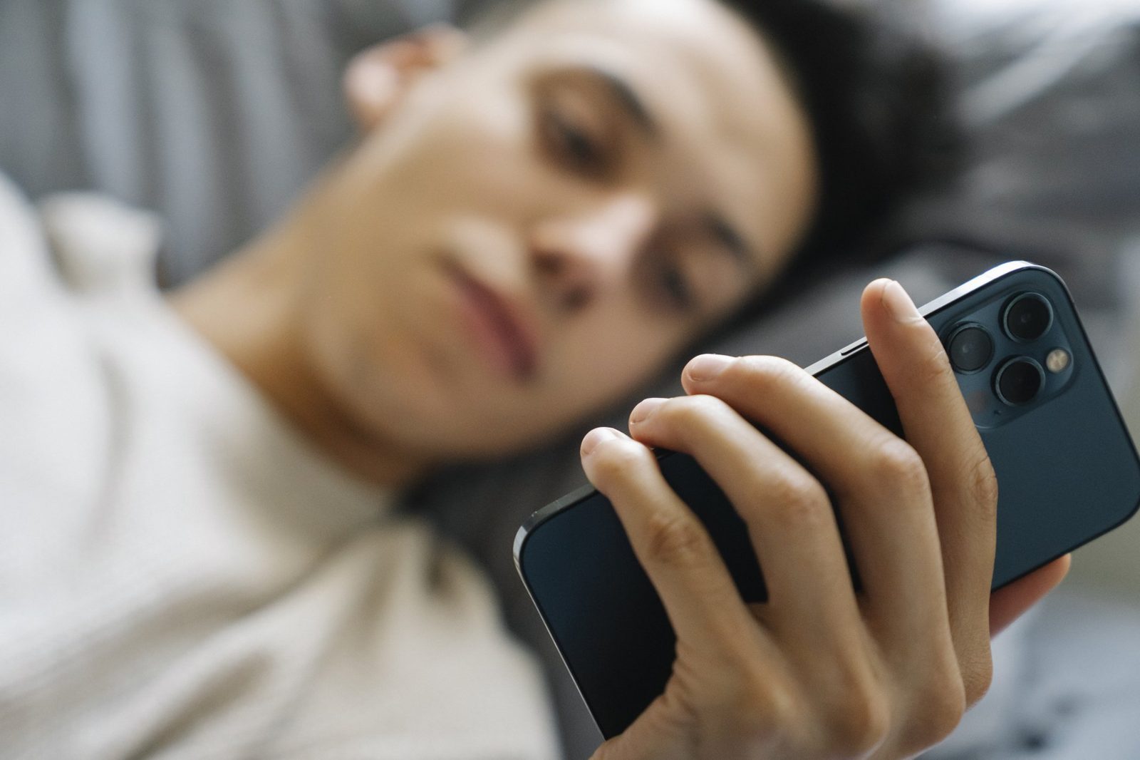 A man is laying on a bed looking at his cell phone.
