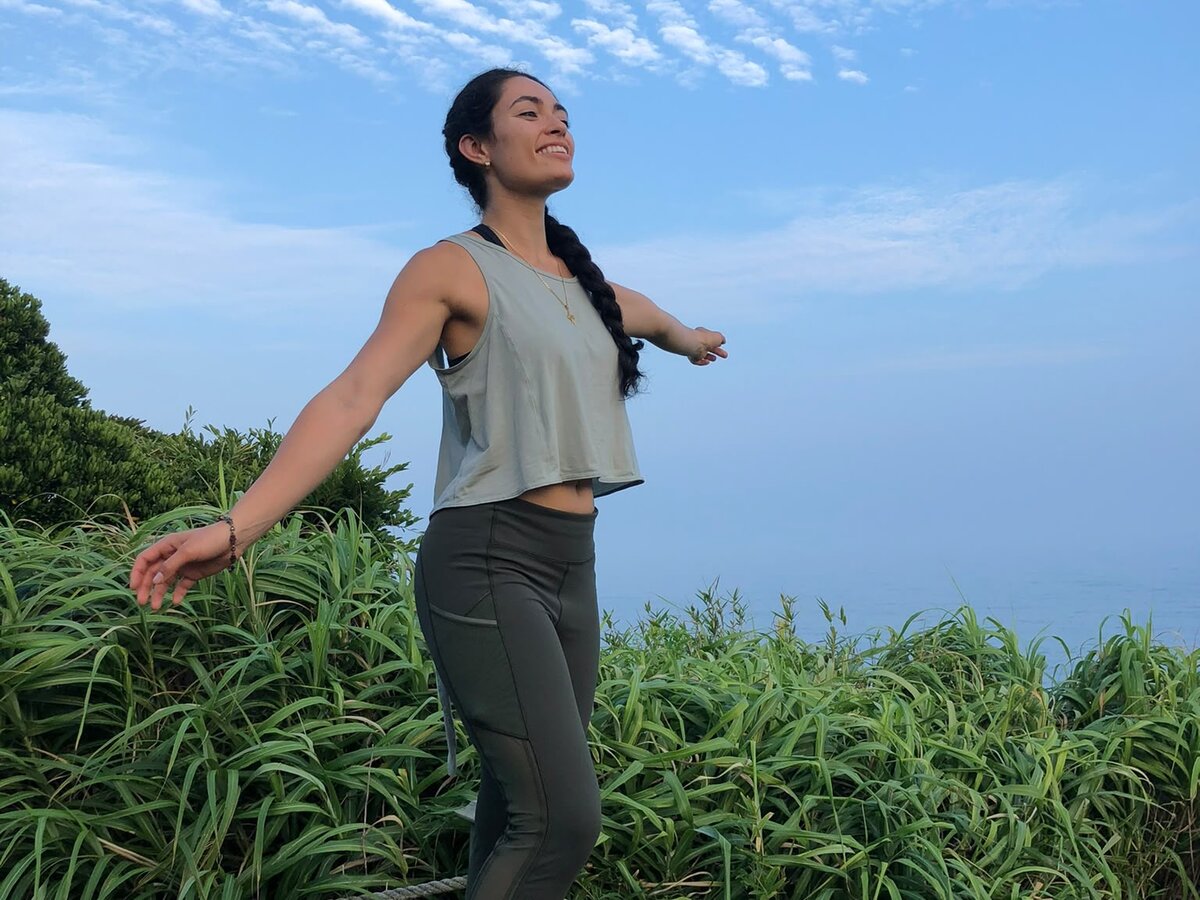 A participant standing with arms open on a coastal cliff at sunrise